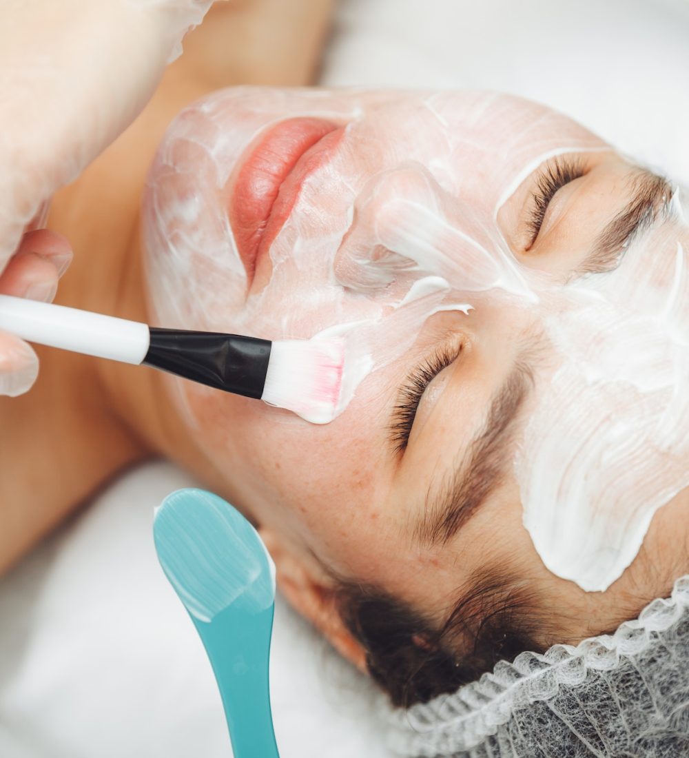 A cosmetologist does facial care and apply a face mask.